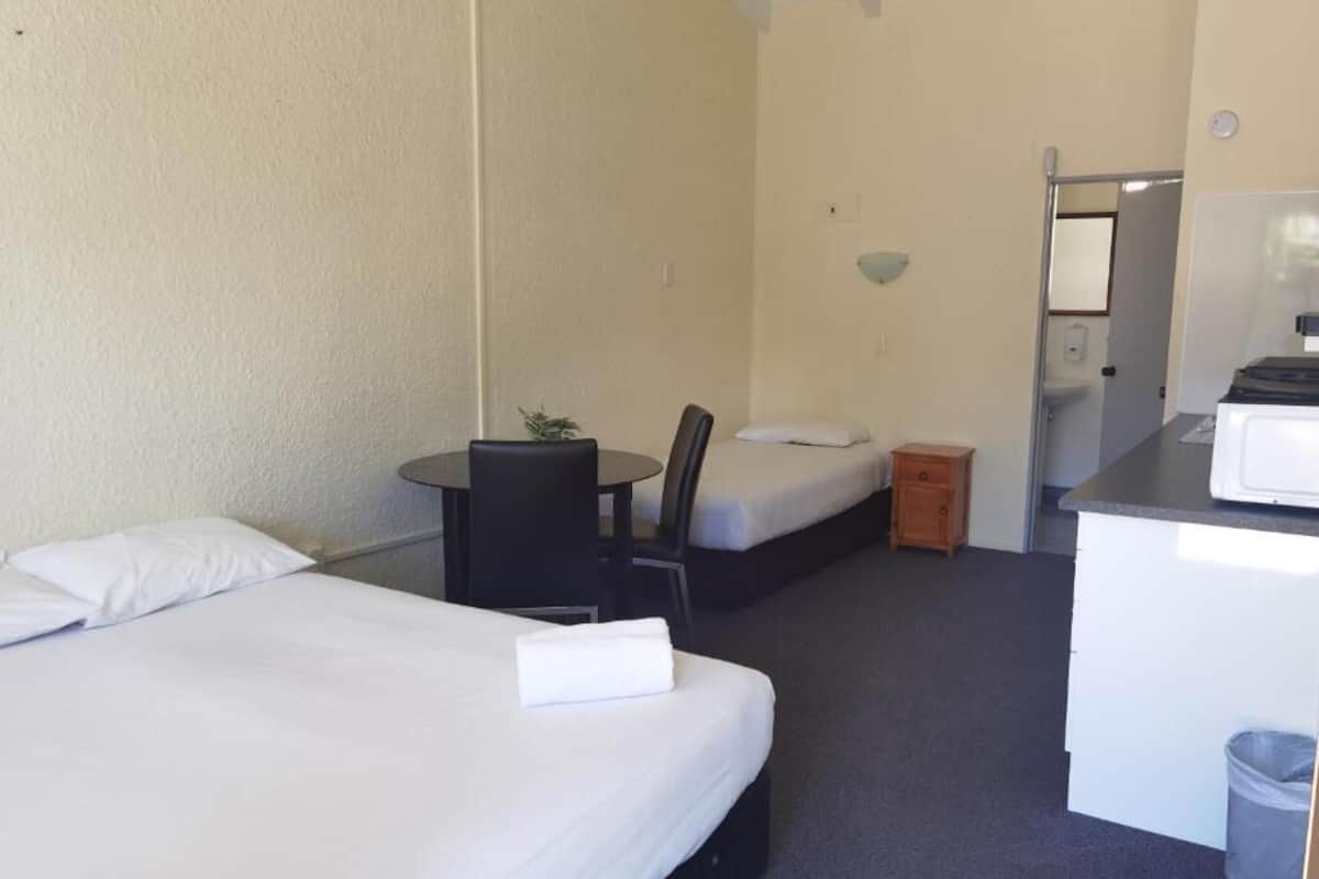 A hotel room with two beds, a small table with a chair, a desk, and a trash bin.
