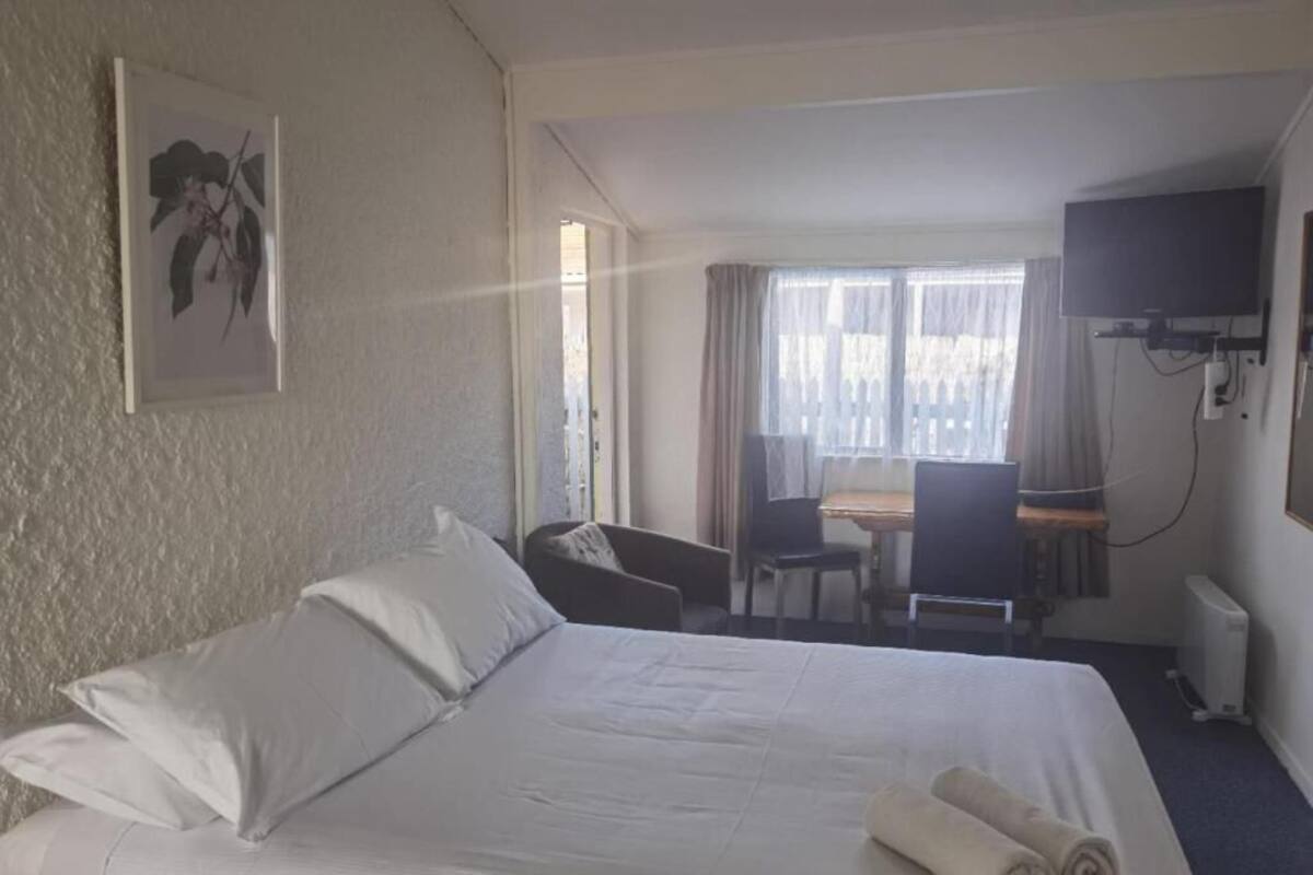 A hotel room with a large bed, a desk, a chair, a television, and a window with curtains.