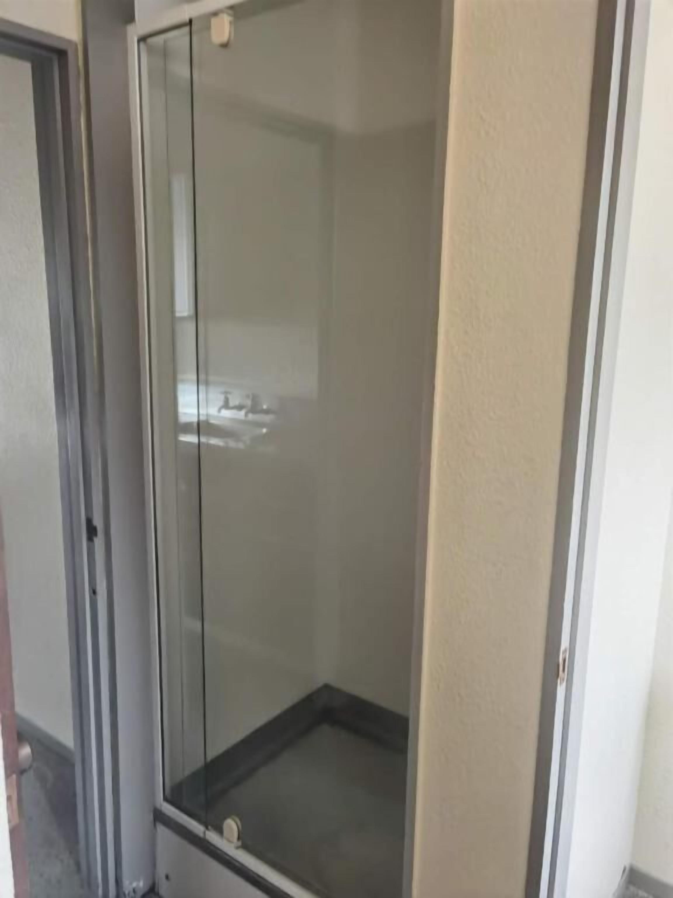 A glass-enclosed shower area with a tiled floor, a visible drain, and a door leading to another room.