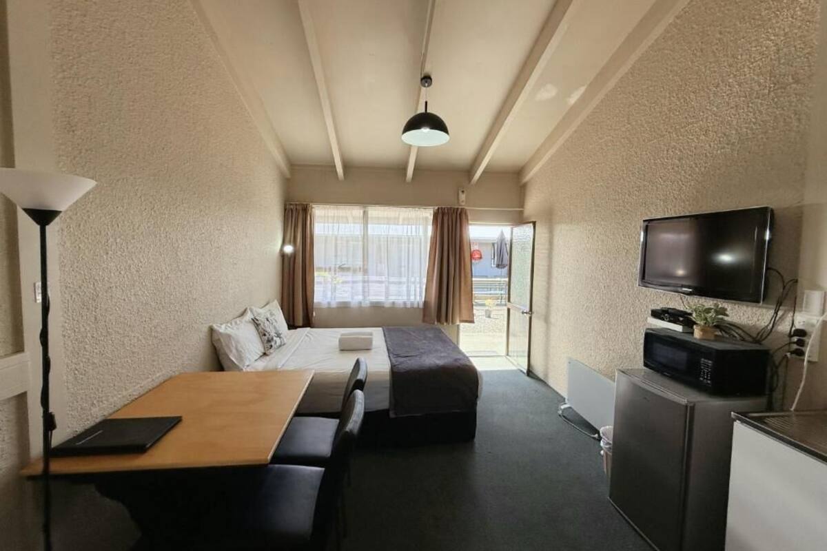 A compact hotel room with a bed, a sofa, a desk, a television, and a microwave.