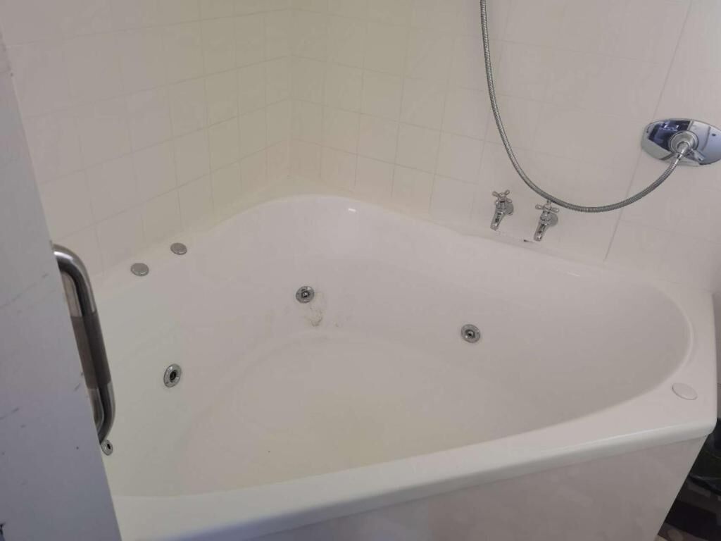 Une baignoire blanche dotée d’un pommeau de douche et de deux robinets.