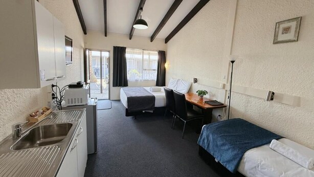 Une chambre d’hôtel compacte comprenant un coin cuisine, un lit, un bureau et un petit espace salon.