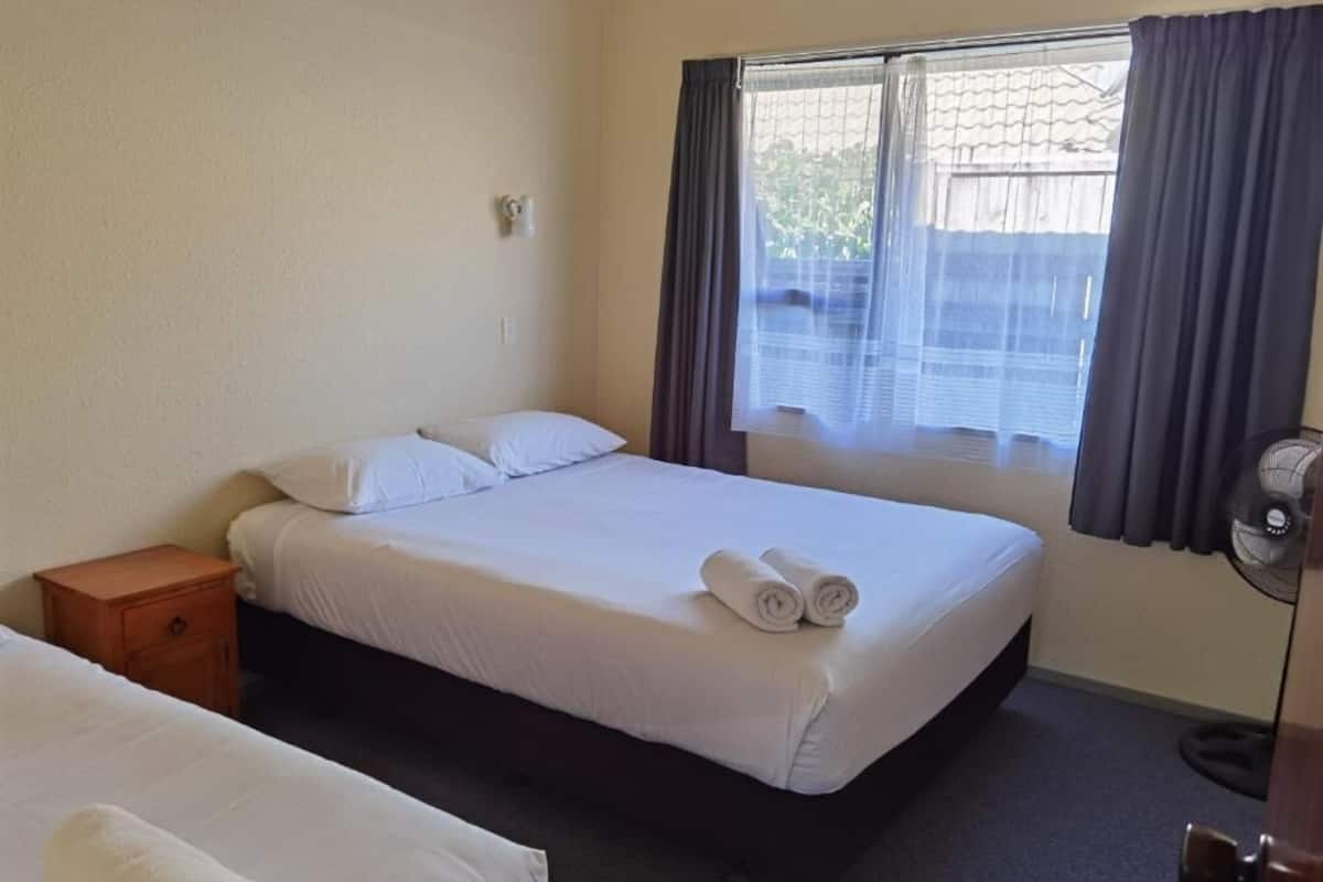 A hotel room with a single bed, a nightstand, a window with curtains, and a fan.