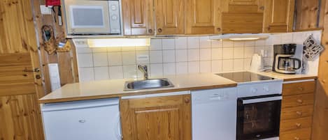 A compact kitchen with wooden cabinets, a microwave, a coffee maker, a dishwasher, and an oven.