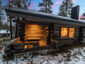 A log cabin with a wooden exterior, a porch with a bench, and a window with curtains.