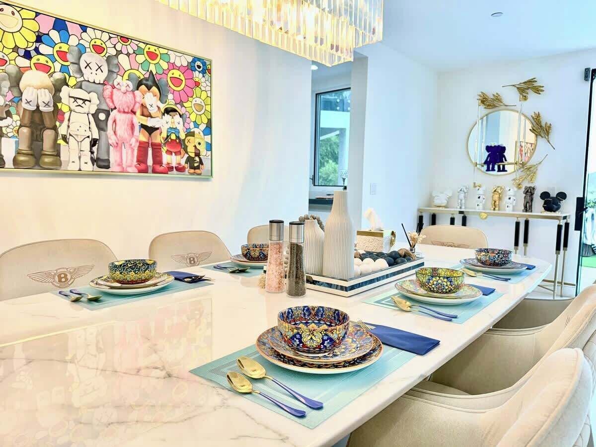 Un comedor con una mesa larga dispuesta para una comida, con cuencos y platos de colores, un florero y un adorno en la pared.