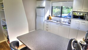 A compact kitchen with a grey countertop, white cabinets, a built-in microwave, and a window with a view of greenery.