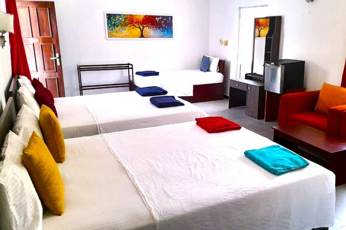 A hotel room with two beds, a red sofa, a TV, and artwork on the walls.