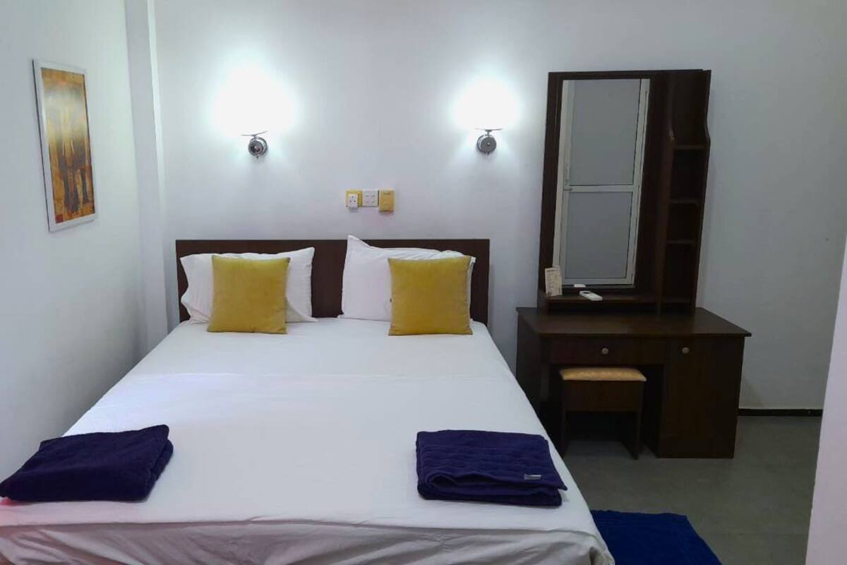 A hotel room with a bed, two bedside tables, a desk, and a mirror.