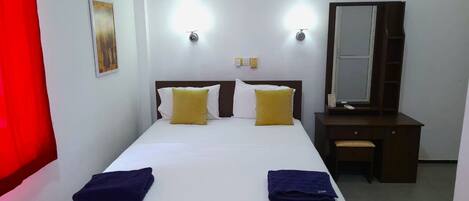 Una habitación de hotel con una cama, dos mesitas de noche, un escritorio y un espejo.