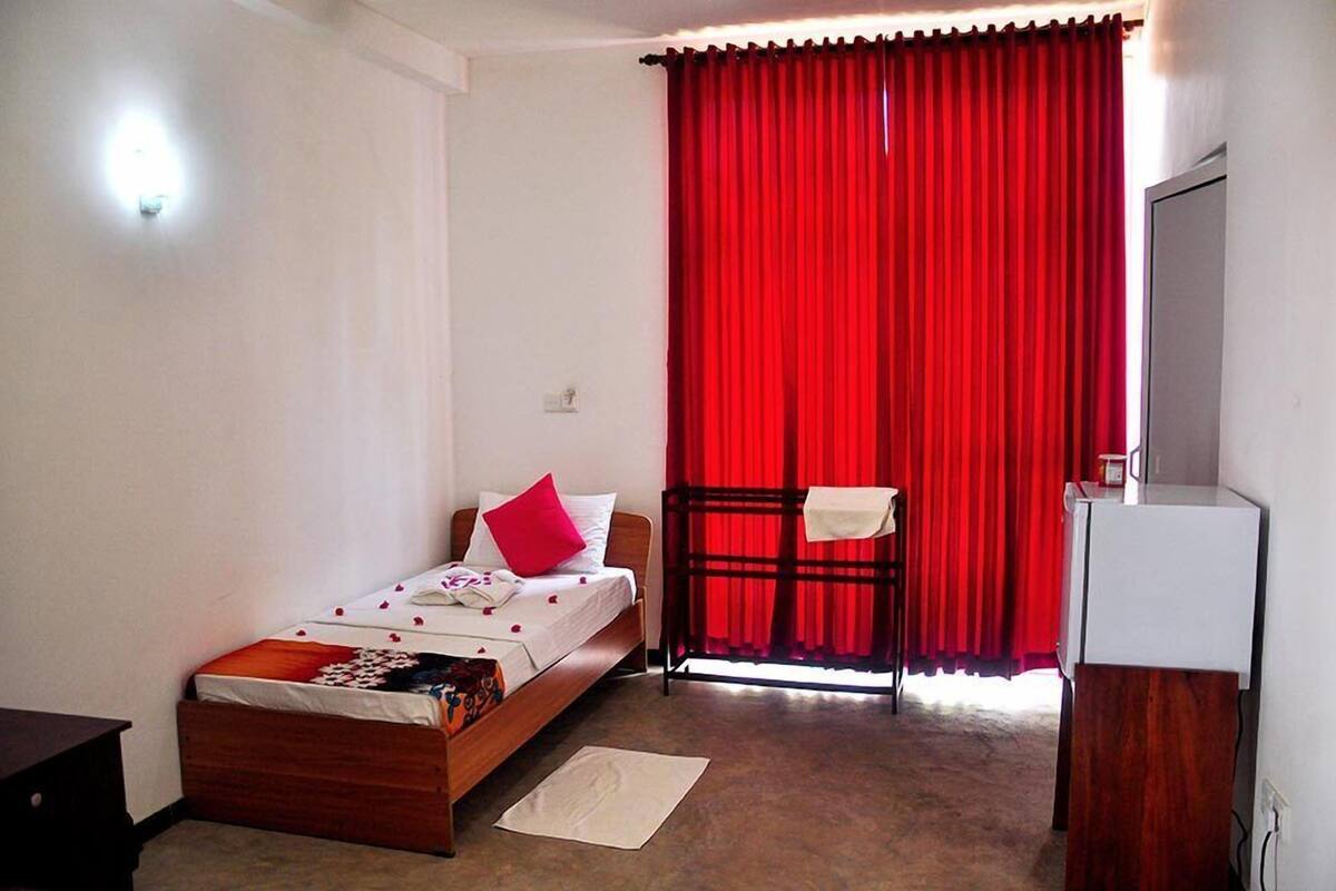 A bedroom with a bed, a red curtain, a white wall, and a white cabinet.