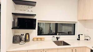 Una cocina moderna con microondas integrado, tostadora y cafetera. Hay un ventanal sobre el fregadero y una encimera con lavaplatos y armarios.