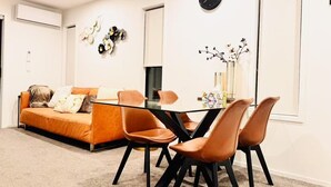 Un moderno salón con una mesa de comedor de cristal, sillas de cuero y un sofá con cojines.
