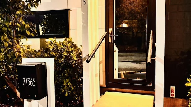 Una entrada de edificio moderna con puerta de vidrio, barandal de madera y buzón con el número 71365.