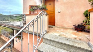 Un edificio con puerta de madera, balcón con barandilla de metal y plantas en macetas.