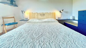 Un dormitorio con una cama grande, dos mesitas de noche, una silla, un aparador y un estante en la pared.