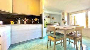 A modern kitchen with white cabinets, a dining table with chairs, and a view of the outside through a window.
