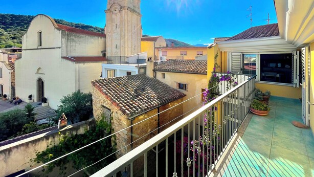 A balcony with a view of a church tower, a yellow building, and a tiled roof.