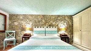 Un dormitorio con pared de piedra, una cama con colcha estampada, dos lámparas de noche, una silla de madera y un armario.