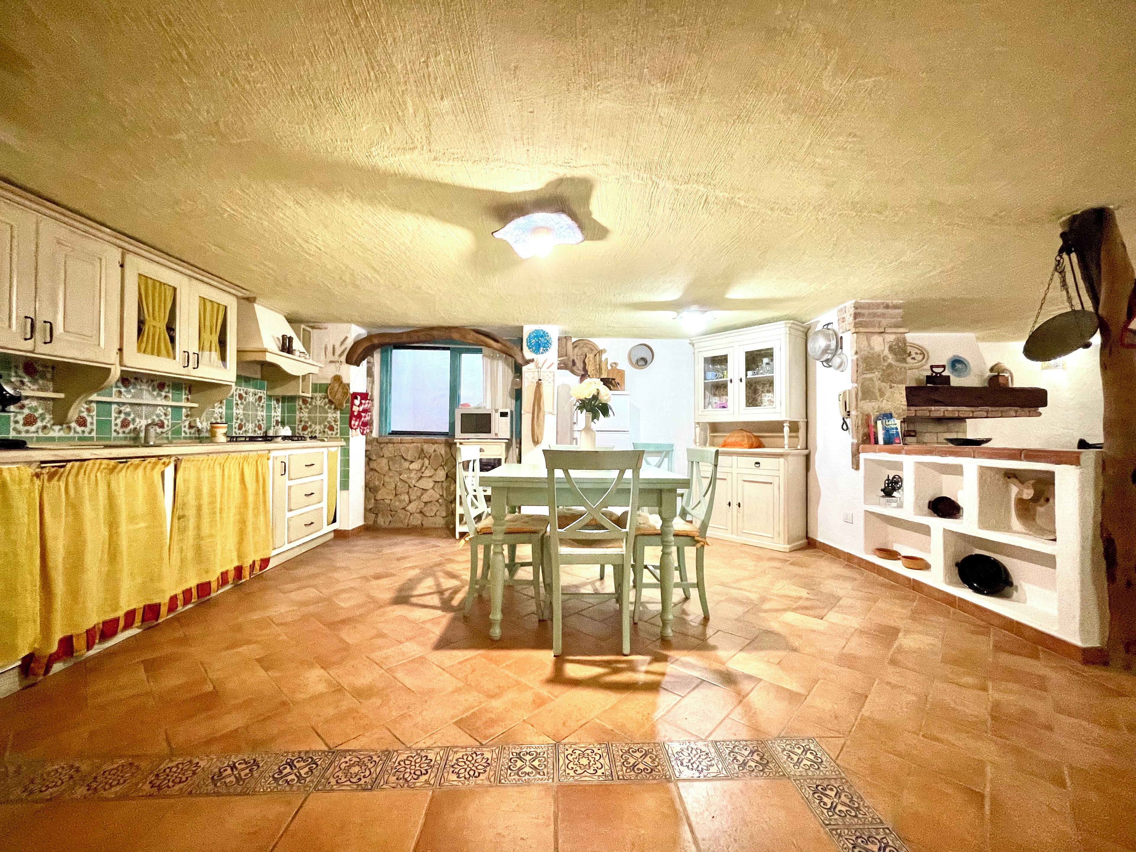 A spacious kitchen with a dining area, stone wall, and tiled floor.