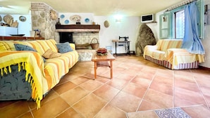 Una sala de estar acogedora con chimenea, sofás a rayas, una máquina de coser y una pared de piedra.