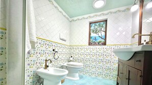 Un baño con dos inodoros blancos, un lavabo y una ventana que da a vistas de árboles y un cuerpo de agua.