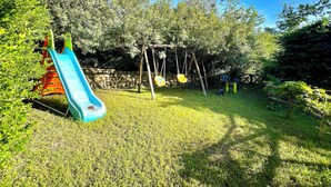 A playground with a slide and swings in a grassy area surrounded by trees. - " Villa Teresa con patio " (Bari Sardo)