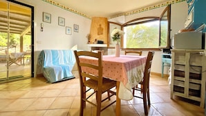 A dining area with a table covered in a pink tablecloth, wooden chairs, a vase with flowers, and a window with a view of greenery. - " Villa Teresa con patio " (Bari Sardo)