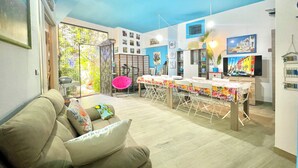 A living room with a sofa, a dining table with chairs, and a kitchen area with a TV. - "  La  Corte   Azzurra  " (Bari Sardo)
