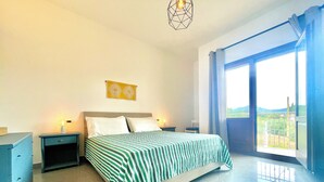 Quarto com cama, mesas de cabeceira, uma obra de arte na parede e uma janela grande com vista.
