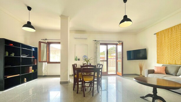 Uma sala ampla com uma mesa de jantar, cadeiras, sofá e televisão na parede.