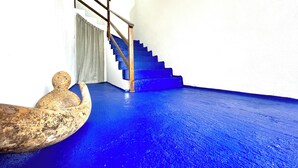 Uma escadaria com degraus azuis e um corrimão de madeira, conduzindo a um patamar com uma parede branca e uma cortina cinzenta.