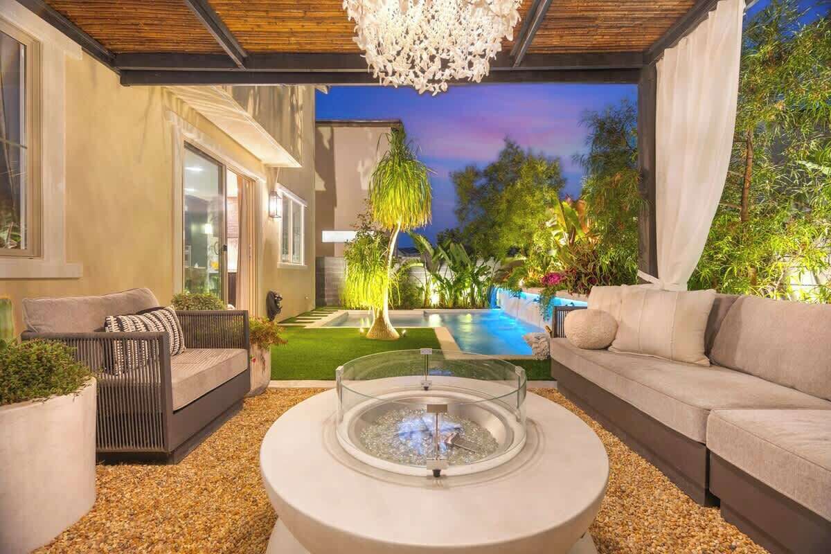 Un espacio exterior moderno con una mesa redonda de vidrio, dos sofás y una piscina al fondo.