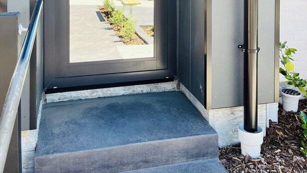 A modern entrance with a glass door, numbered 103, leading to a courtyard with benches and plants. - Heartstay Studio CBD, CHC (Christchurch)