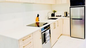 A modern kitchen with light wood cabinets, a white countertop, a built-in oven, and a stainless steel refrigerator. - Heartstay Studio CBD, CHC (Christchurch)