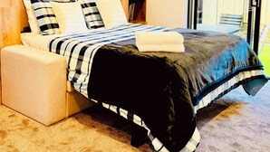 A modern bedroom with a wooden headboard, a bed with striped bedding, and a view of the outside through a glass door. - Heartstay Studio CBD, CHC (Christchurch)