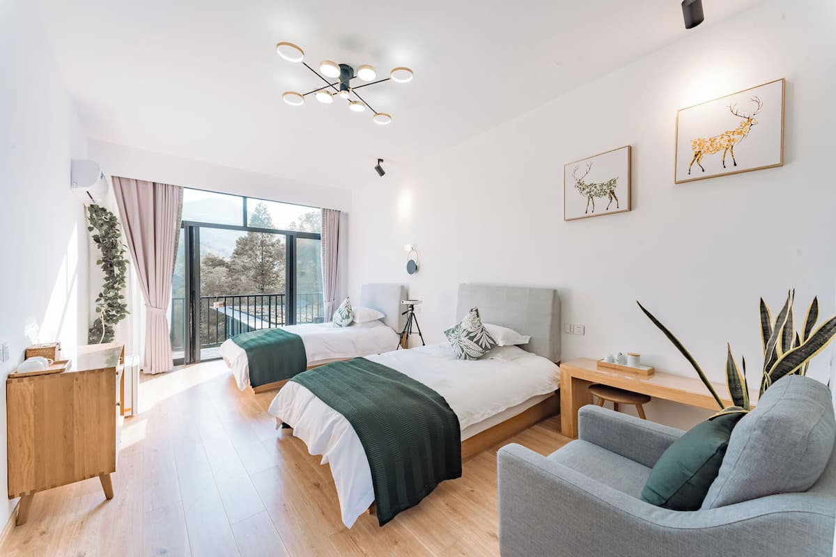 A modern bedroom with two beds, a desk, a chair, and a balcony with a view.