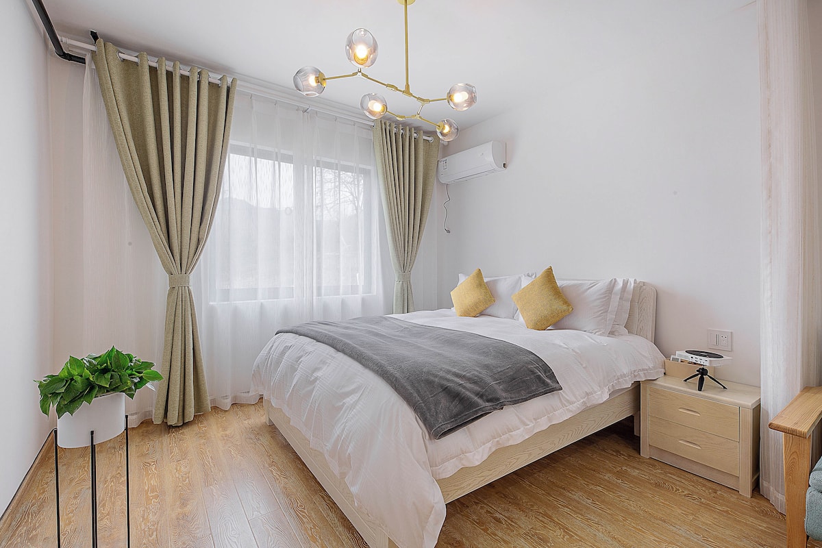 A bedroom with a bed, bedside table, and a plant.