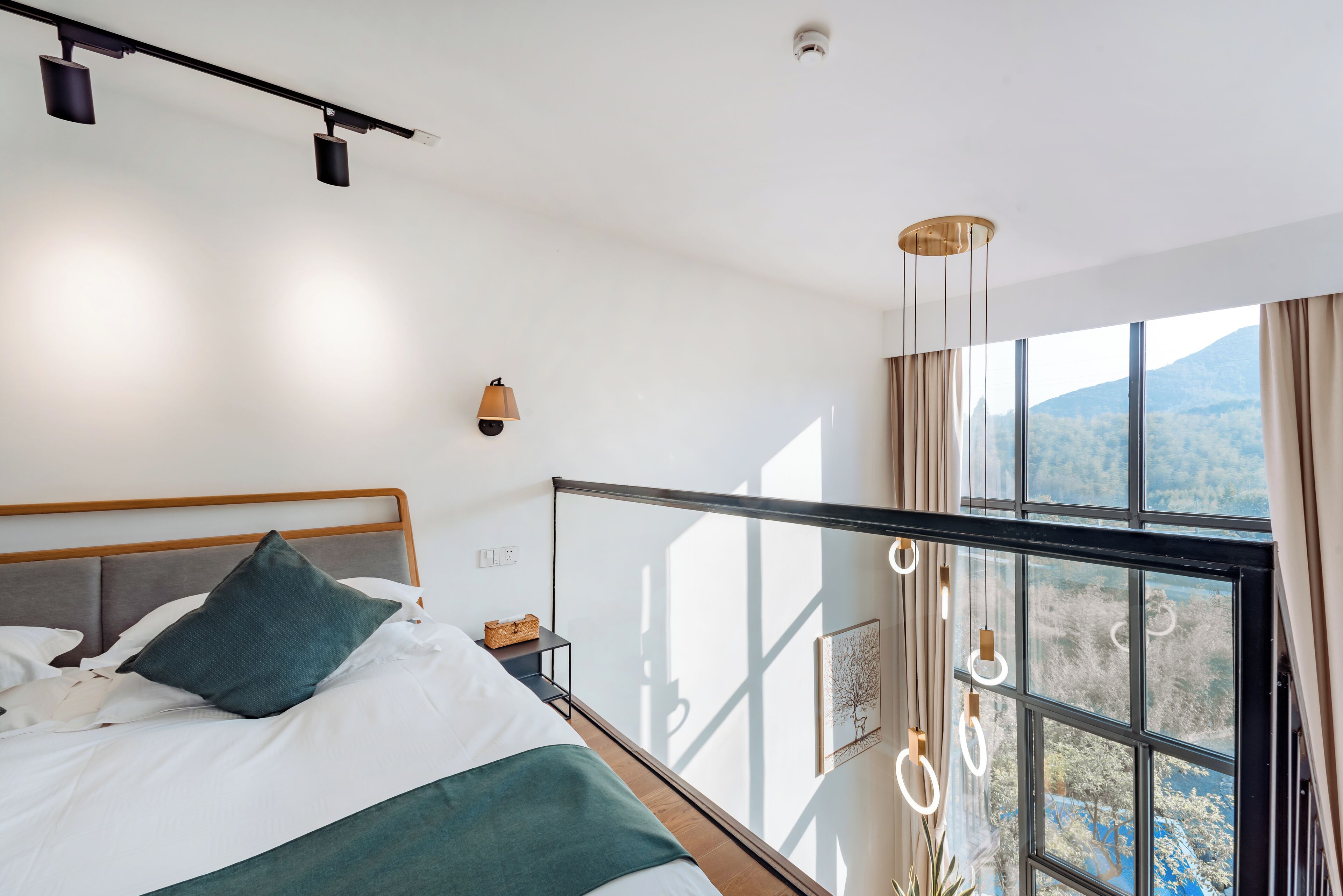 A modern hotel room with a large bed, a view of the outdoors through a balcony, and a ceiling light fixture.