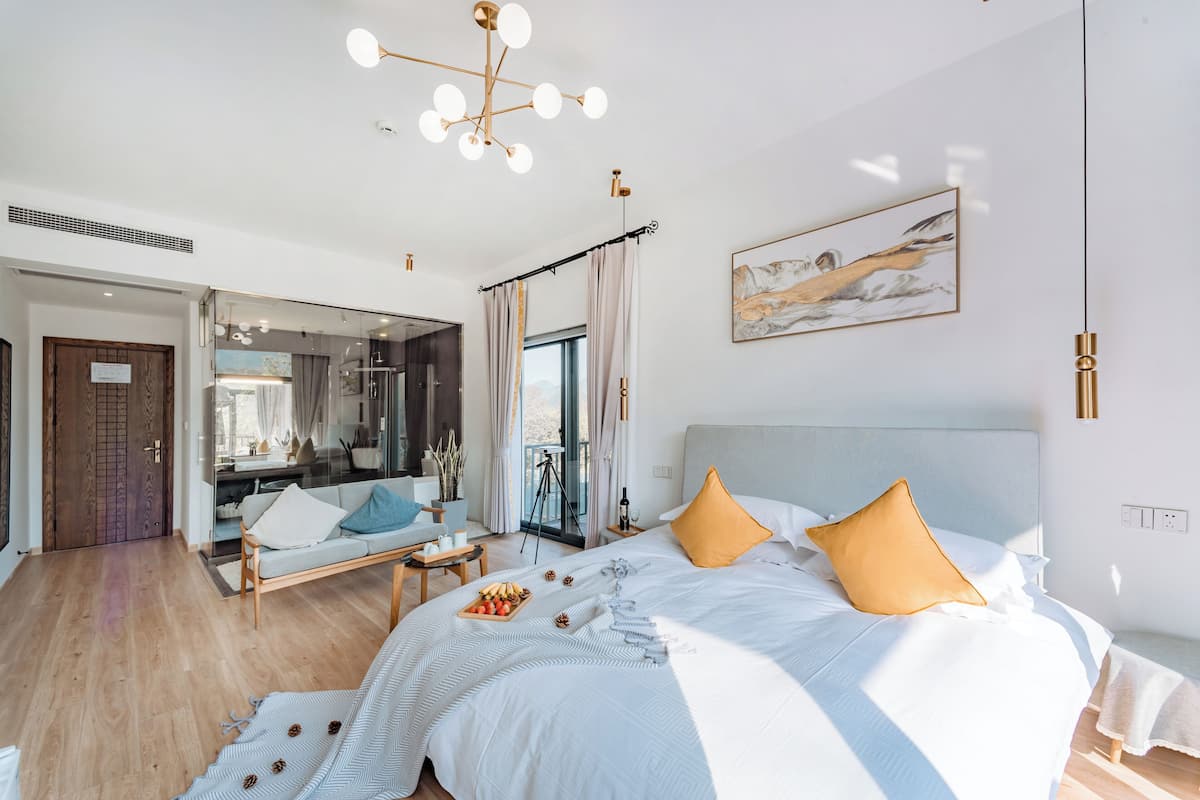 A modern bedroom with a large bed, a sofa, a dining table, and a balcony.