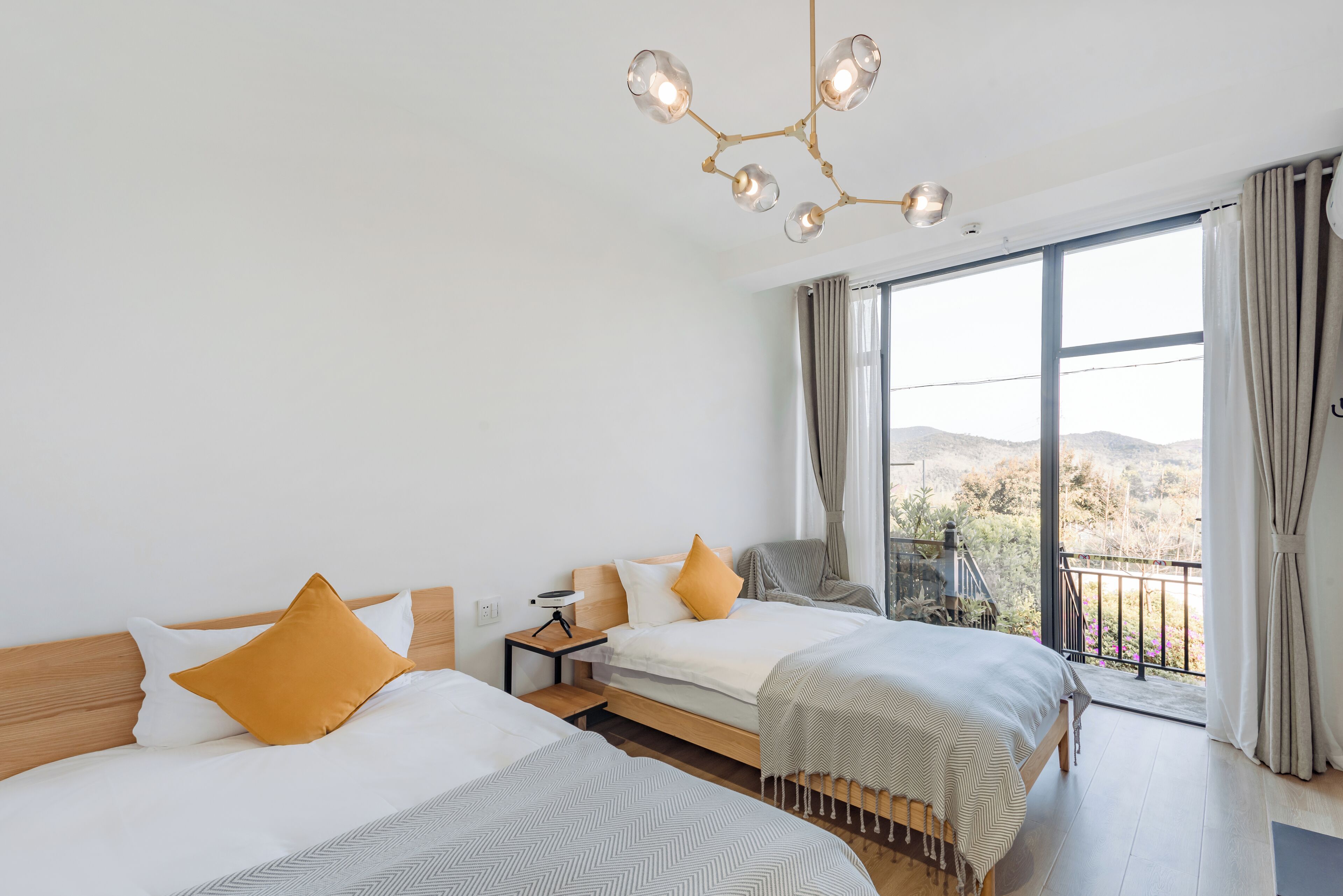 Quarto de hotel com duas camas, varanda e vista, além de um lustre moderno.
