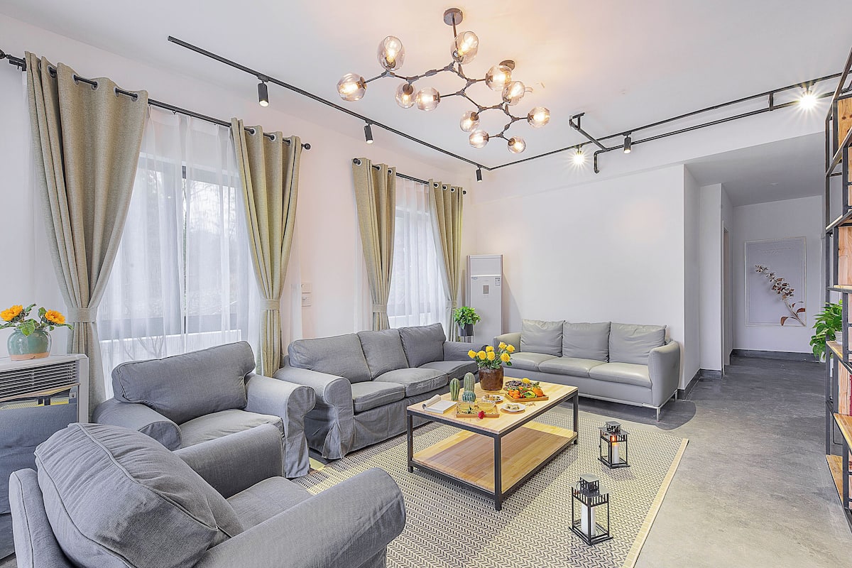 A modern living room with grey sofas, a wooden coffee table, and a chandelier.