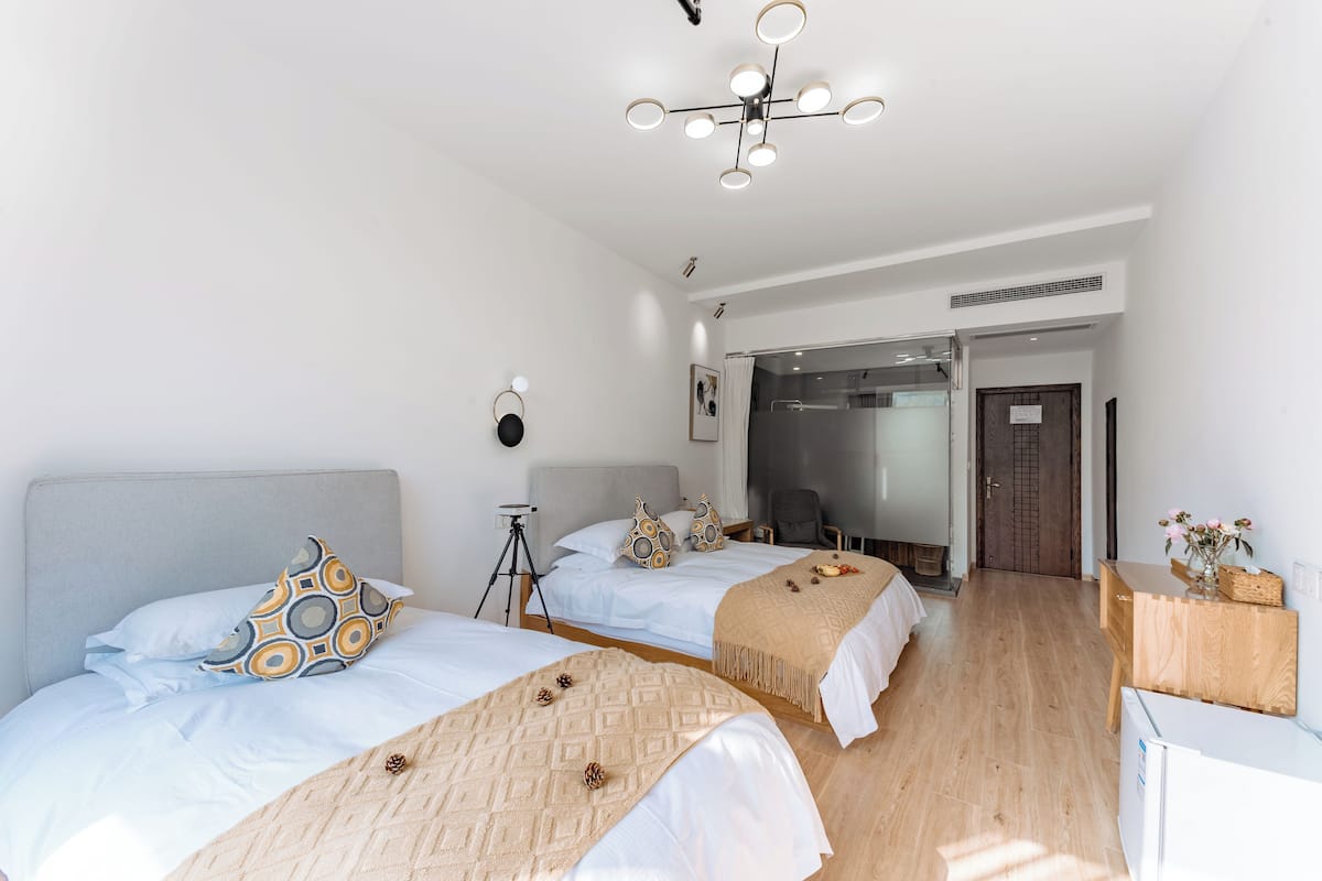 A hotel room with two beds, a ceiling light, a desk, and a door leading to a bathroom.