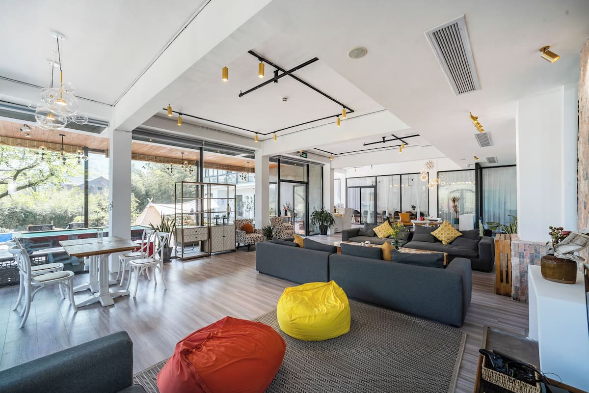 A spacious living area with a large sofa, a yellow bean bag, and a dining area with white chairs and a wooden table.