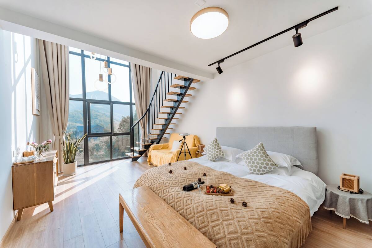 A modern bedroom with a large bed, a wooden bench, a desk, and a tripod.