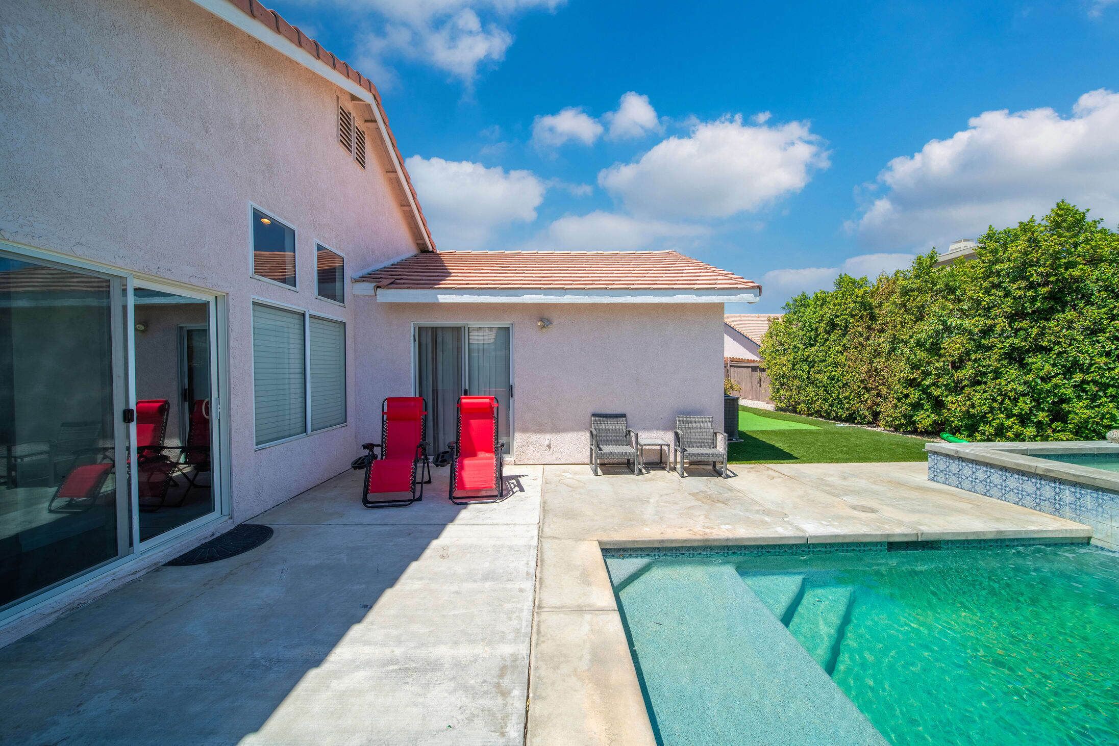 A modern house with a swimming pool, red and gray outdoor furniture, and a well-maintained lawn.