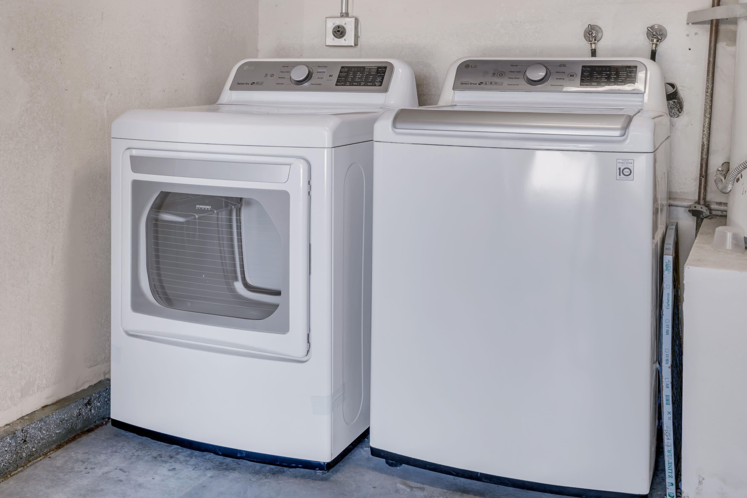 Two white front-loading washing machines in a laundry area with a concrete floor and a plain wall.