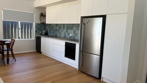 A modern kitchen with white cabinets, a stainless steel refrigerator, and a wooden dining table. - The Front House (Augusta)