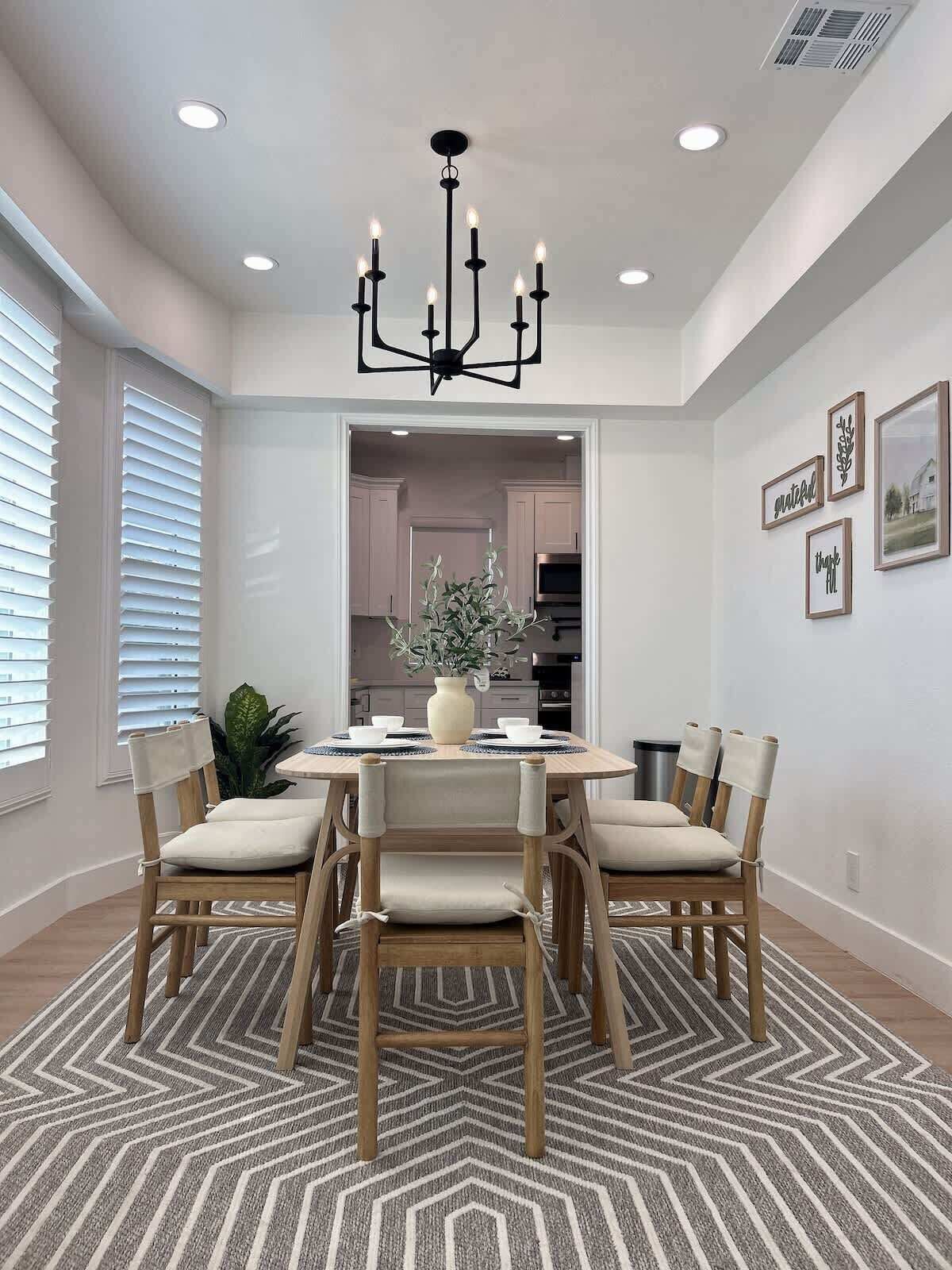 A dining area with a round table, six chairs, a chandelier, and a patterned rug.