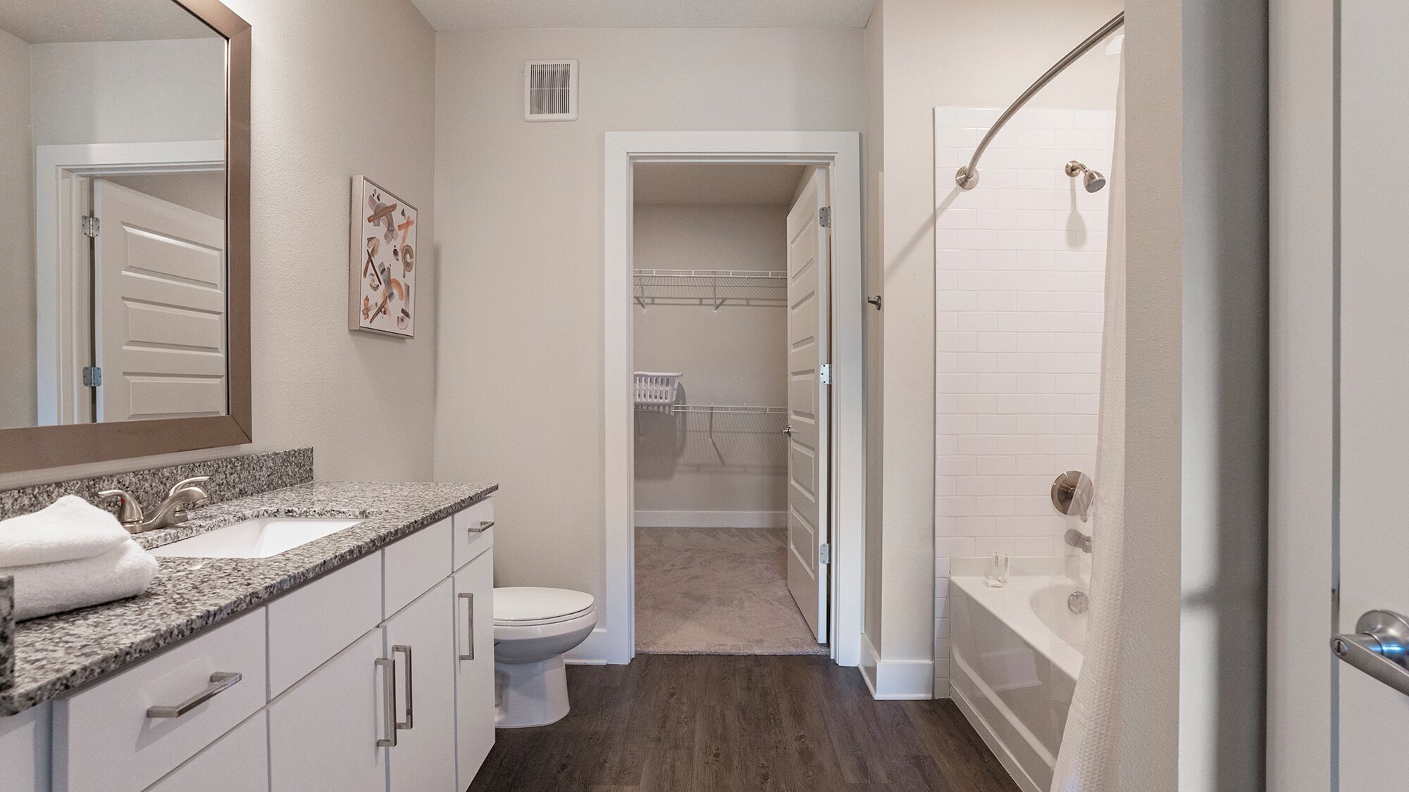 Un baño moderno con lavamanos de granito, inodoro y ducha a ras de suelo con puerta de vidrio.
